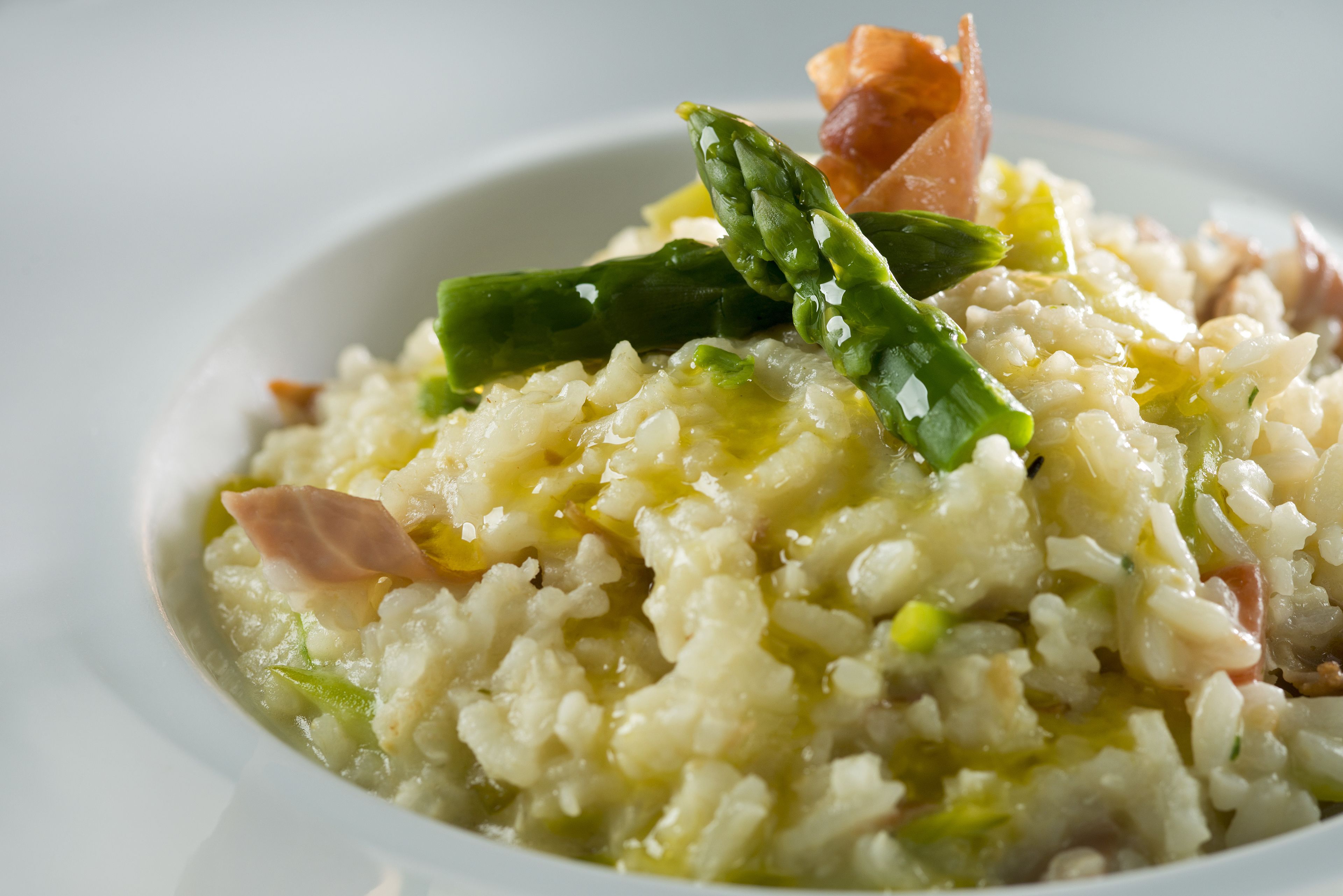 A bowl of risotto with asparagus and a piece of salmon.