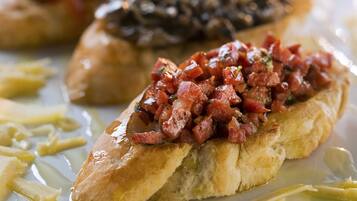 Un plato de bruschetta con tomate y hierbas picadas, acompañado de una salsa cremosa y algunas verduras encurtidas.