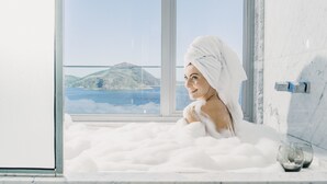 Una persona en una bañera llena de burbujas, con vistas a un paisaje montañoso a través de una ventana.