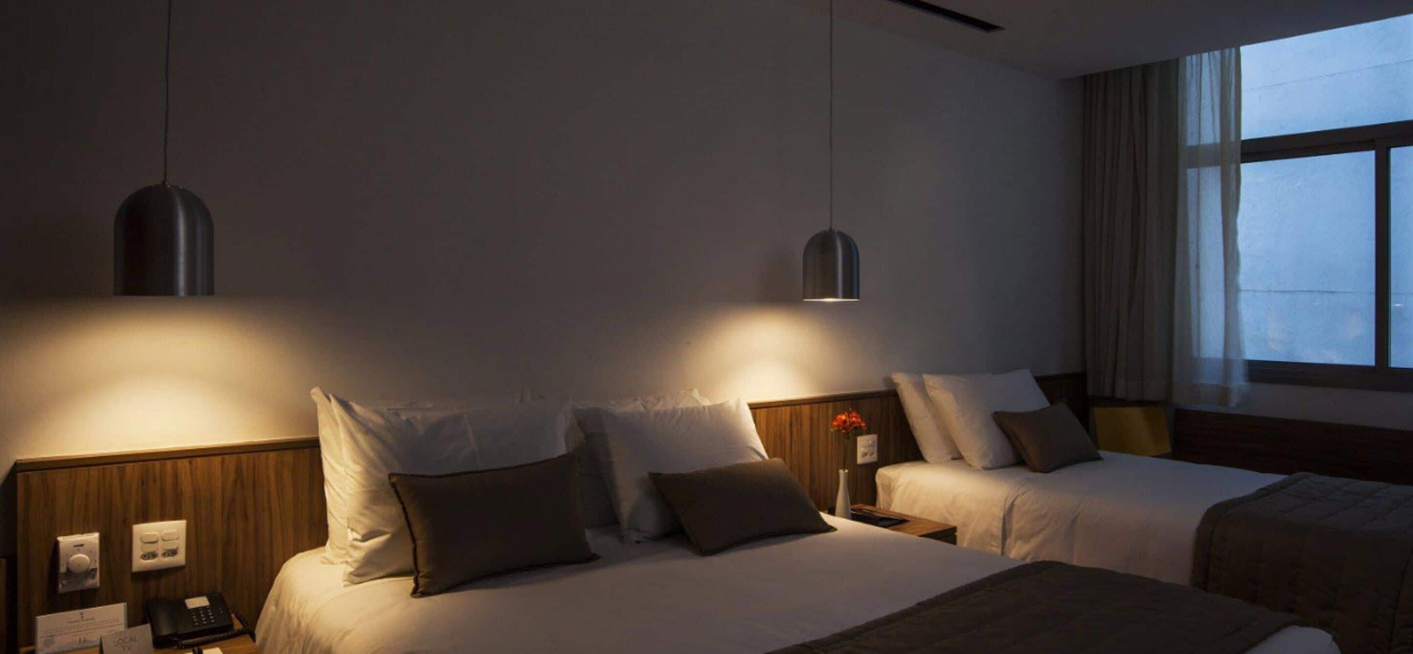 Habitación de hotel con dos camas, una mesita de noche con teléfono y lámpara, y una ventana con cortinas.