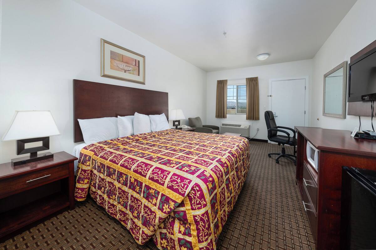A hotel room with a large bed, a desk with a computer, a chair, a TV, and a window with curtains.