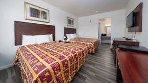 A hotel room with two beds, a desk, a television, and artwork on the walls. - America Inn & Suites (Ridgecrest)