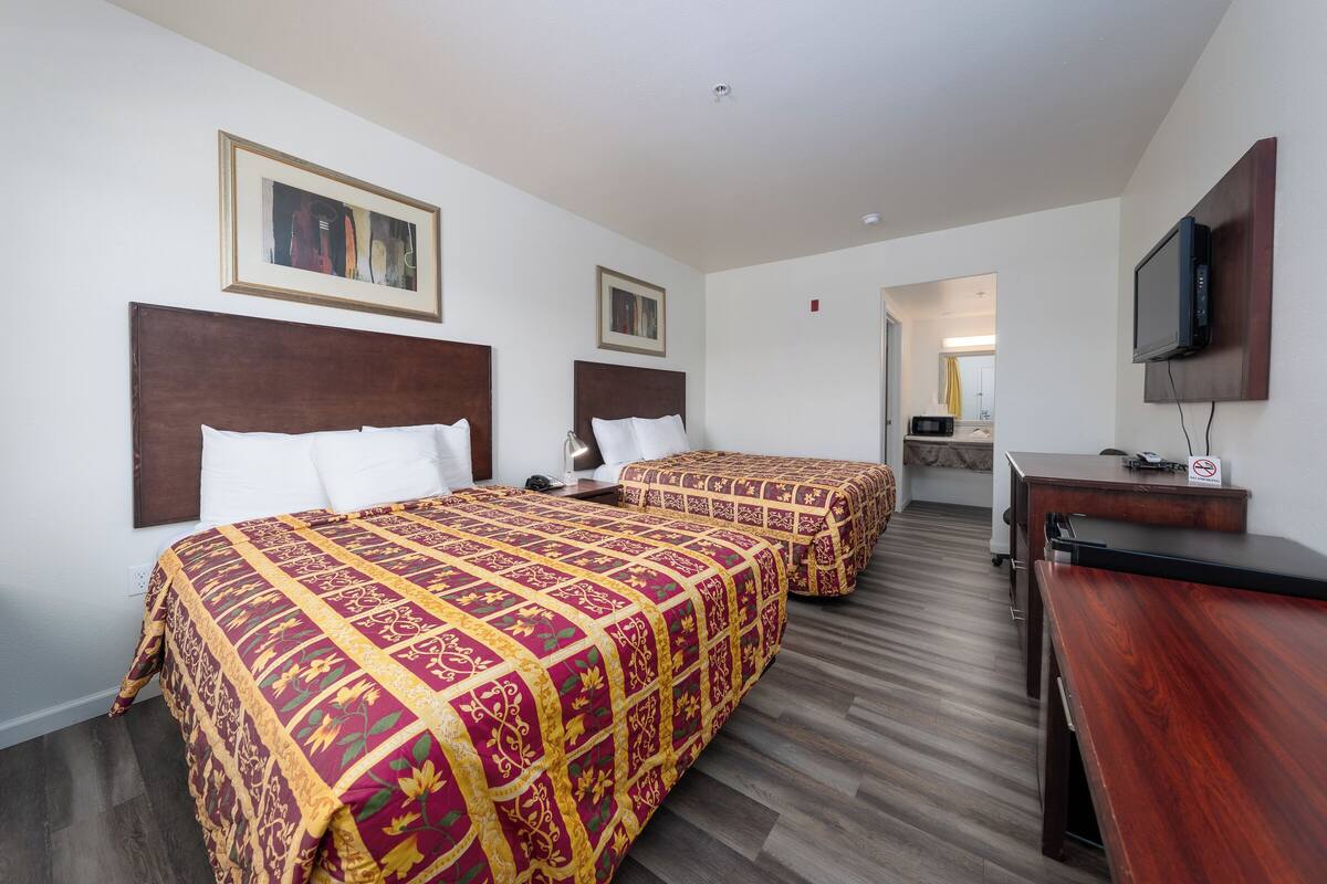 A hotel room with two beds, a desk, a television, and artwork on the walls.