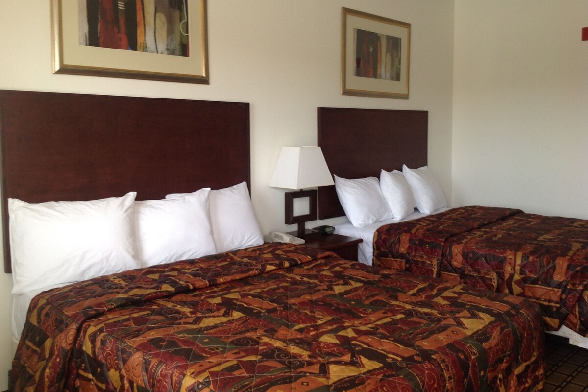 A hotel room with two beds, each with a headboard, a bedside table with a lamp, and two framed pictures on the wall.