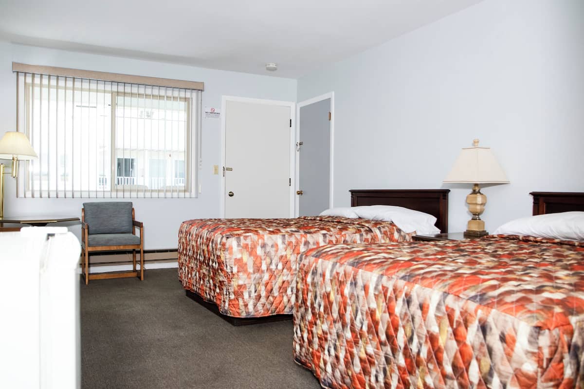 Hotellihuone, jossa on kaksi sänkyä, tuoli, työpöytä ja lamppu.
