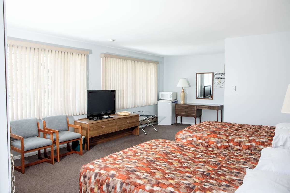 Hotellihuone, jossa on kaksi sänkyä, televisio, työpöytä lampun kanssa ja tuoli.