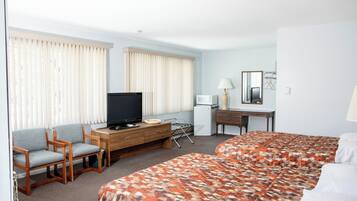 A hotel room with two beds, a TV, a desk with a lamp, and a chair.
