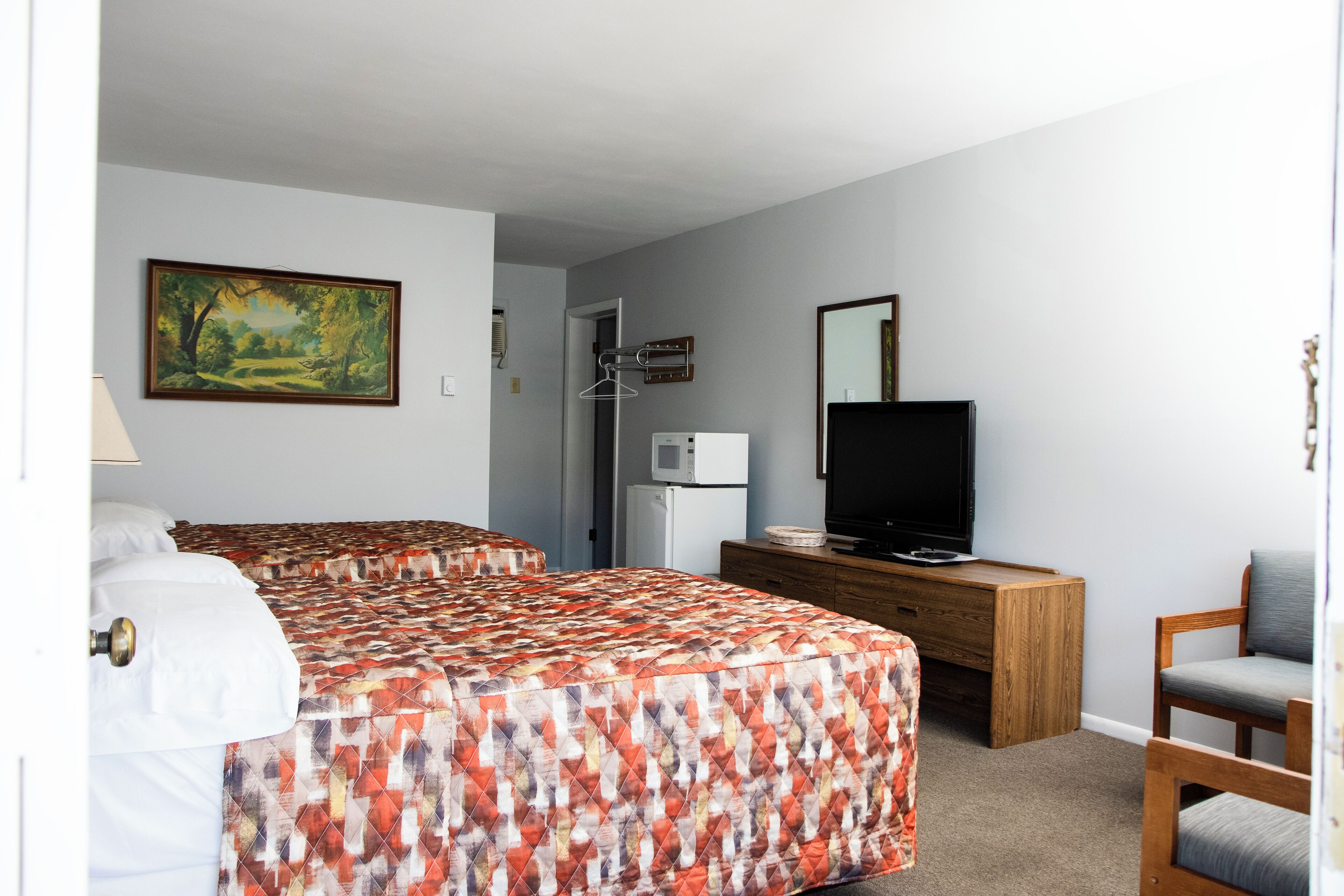 A bedroom with a bed, dresser, TV, and a painting on the wall.