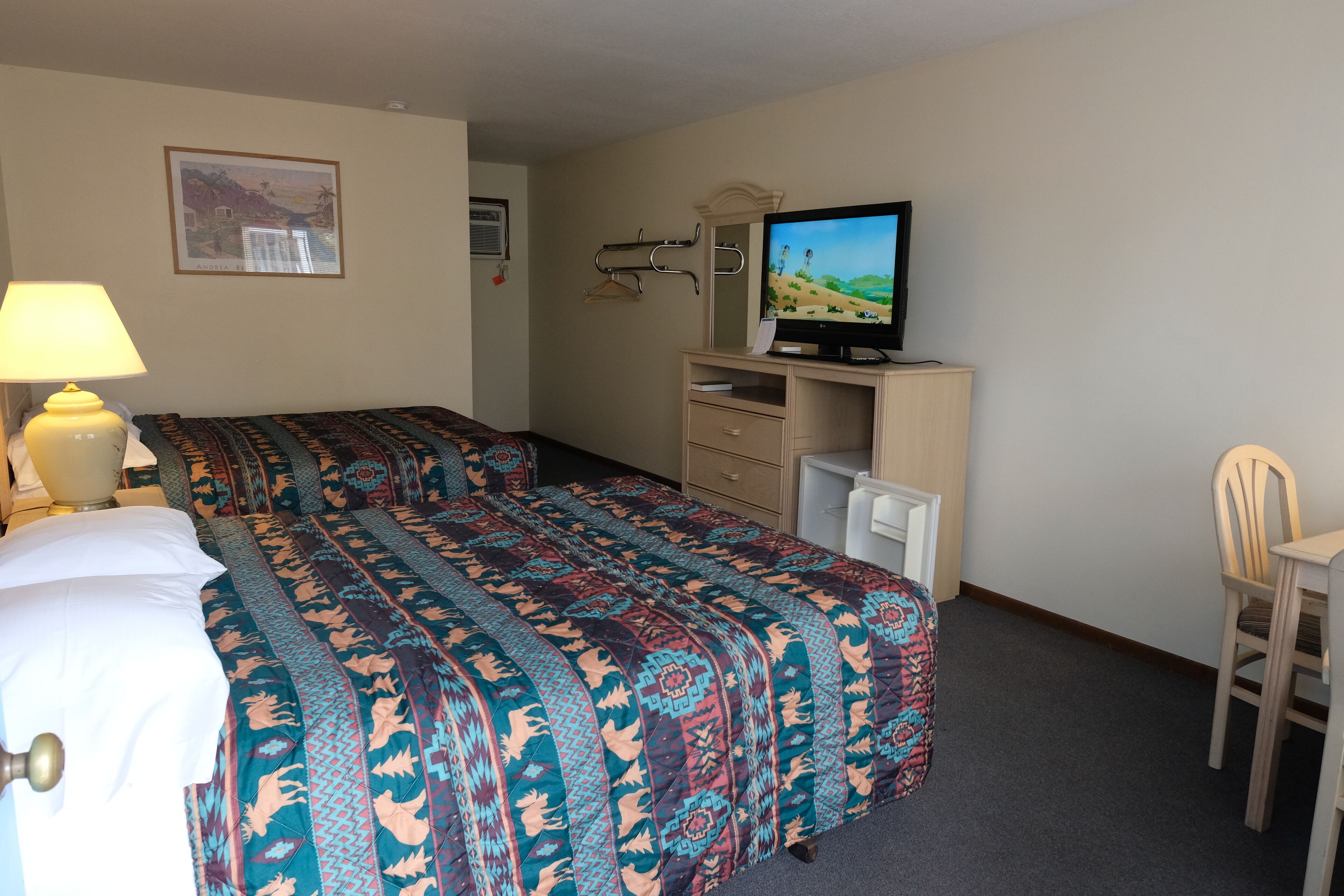 A hotel room with two beds, a television, a desk, and a chair.
