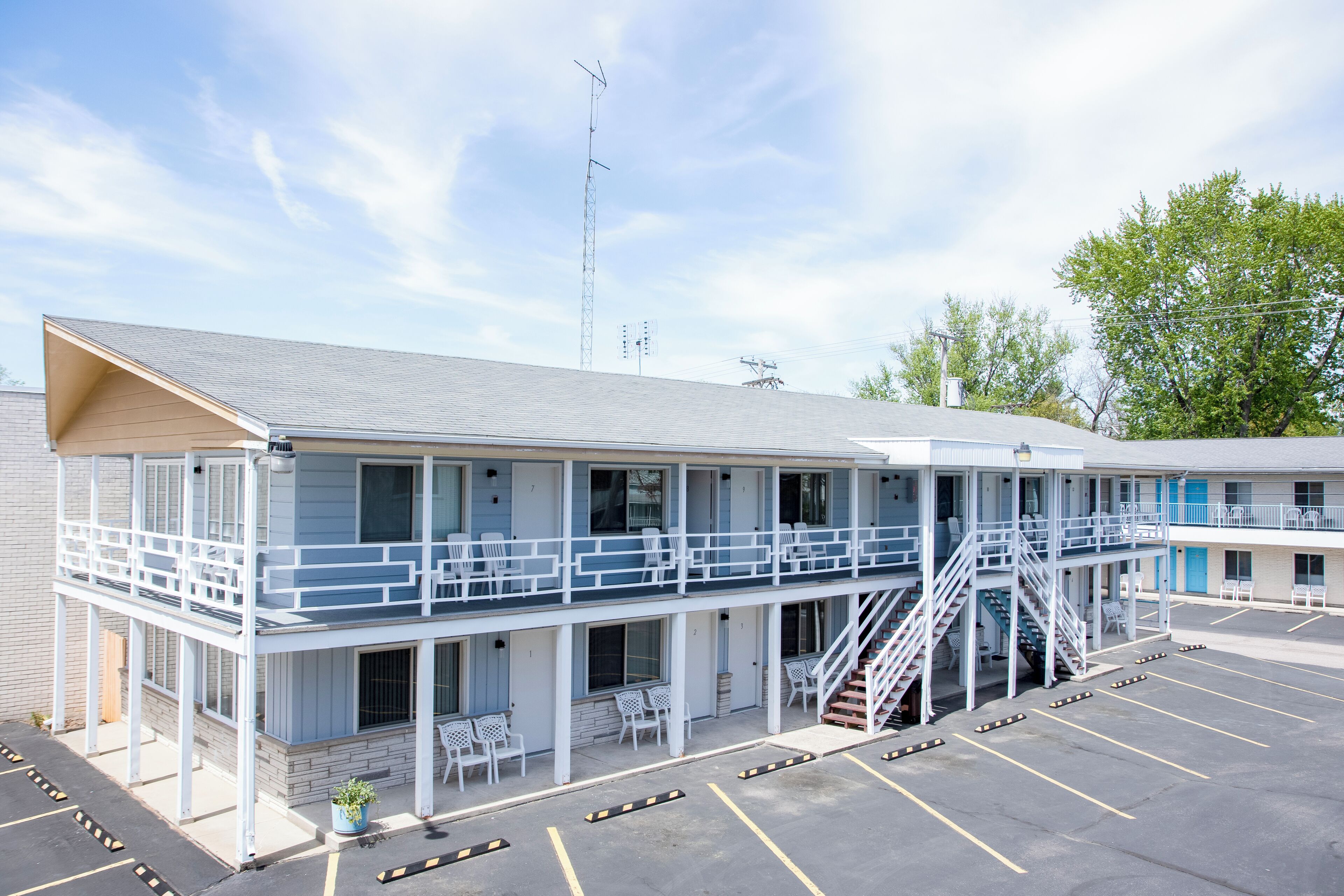 Un motel con una estructura de dos pisos, un área de estar al aire libre techada y un estacionamiento.