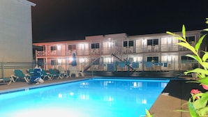 A swimming pool with lounge chairs and a building with multiple floors in the background. - Starlite Motel (Wisconsin Dells)