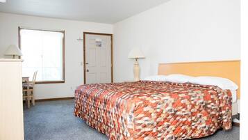 A bedroom with a bed, a desk, a chair, a lamp, and a door.