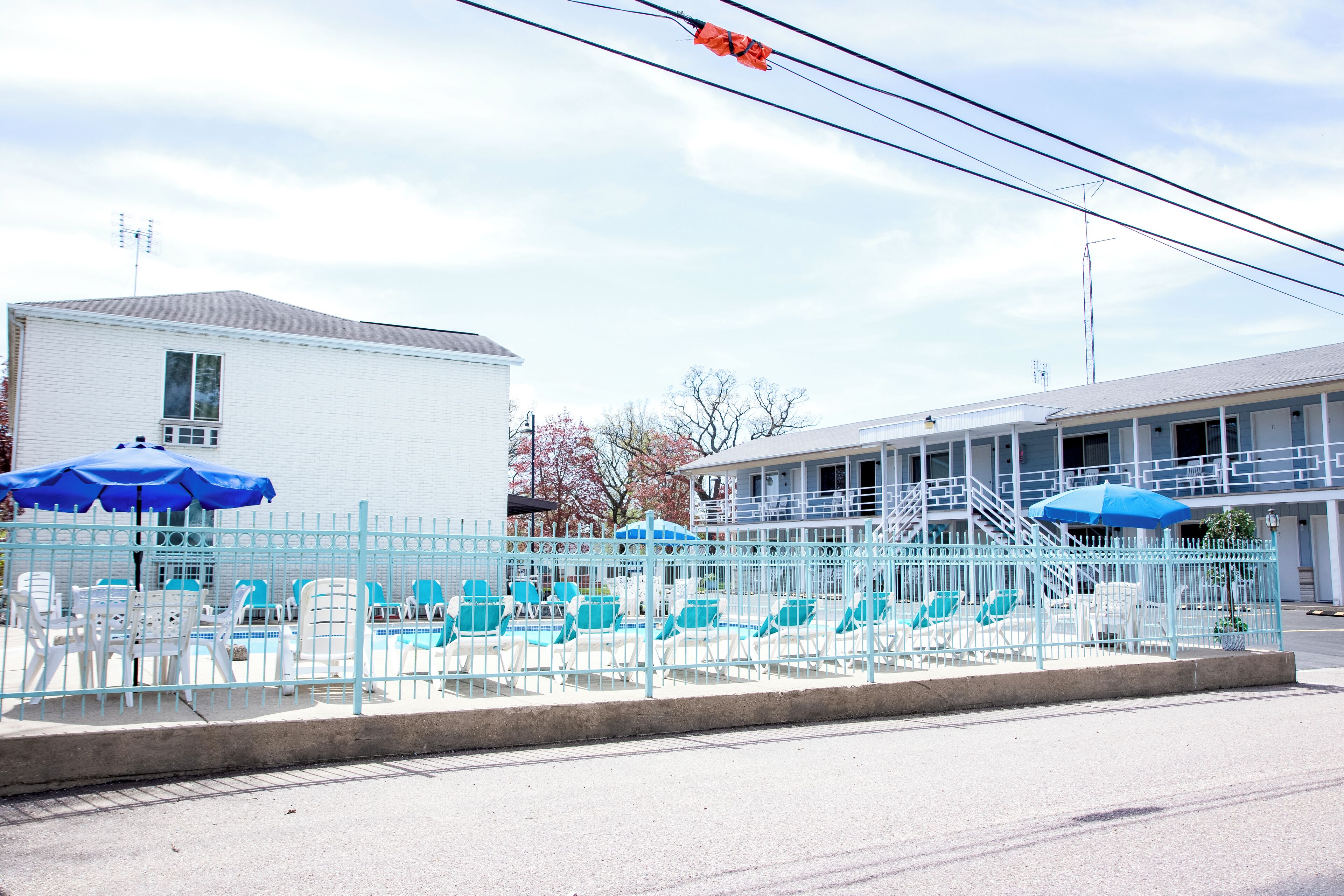 A motel with a fenced pool area, outdoor seating, and a staircase leading to the entrance.