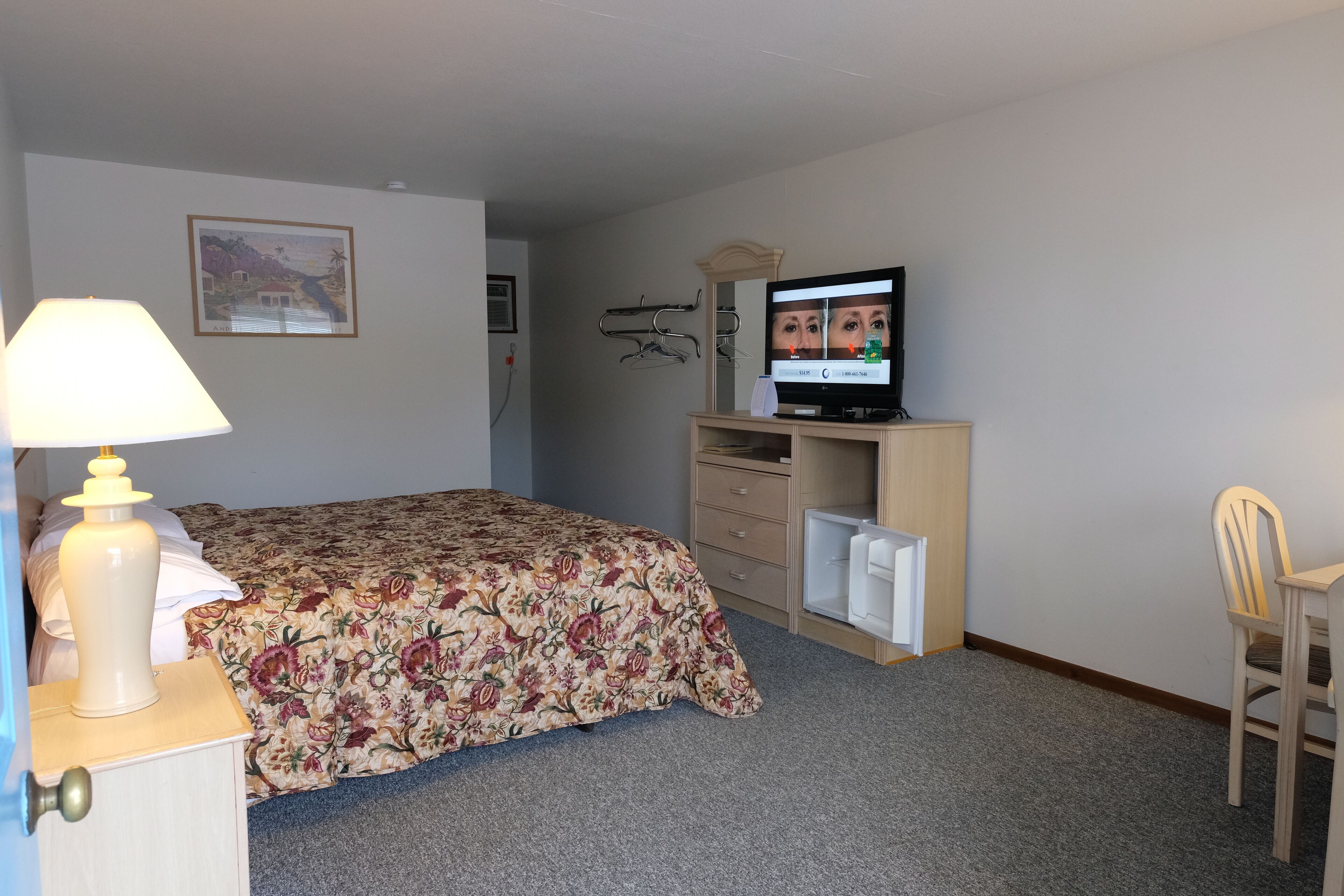 A hotel room with a bed, a desk, a chair, a television, and a lamp.
