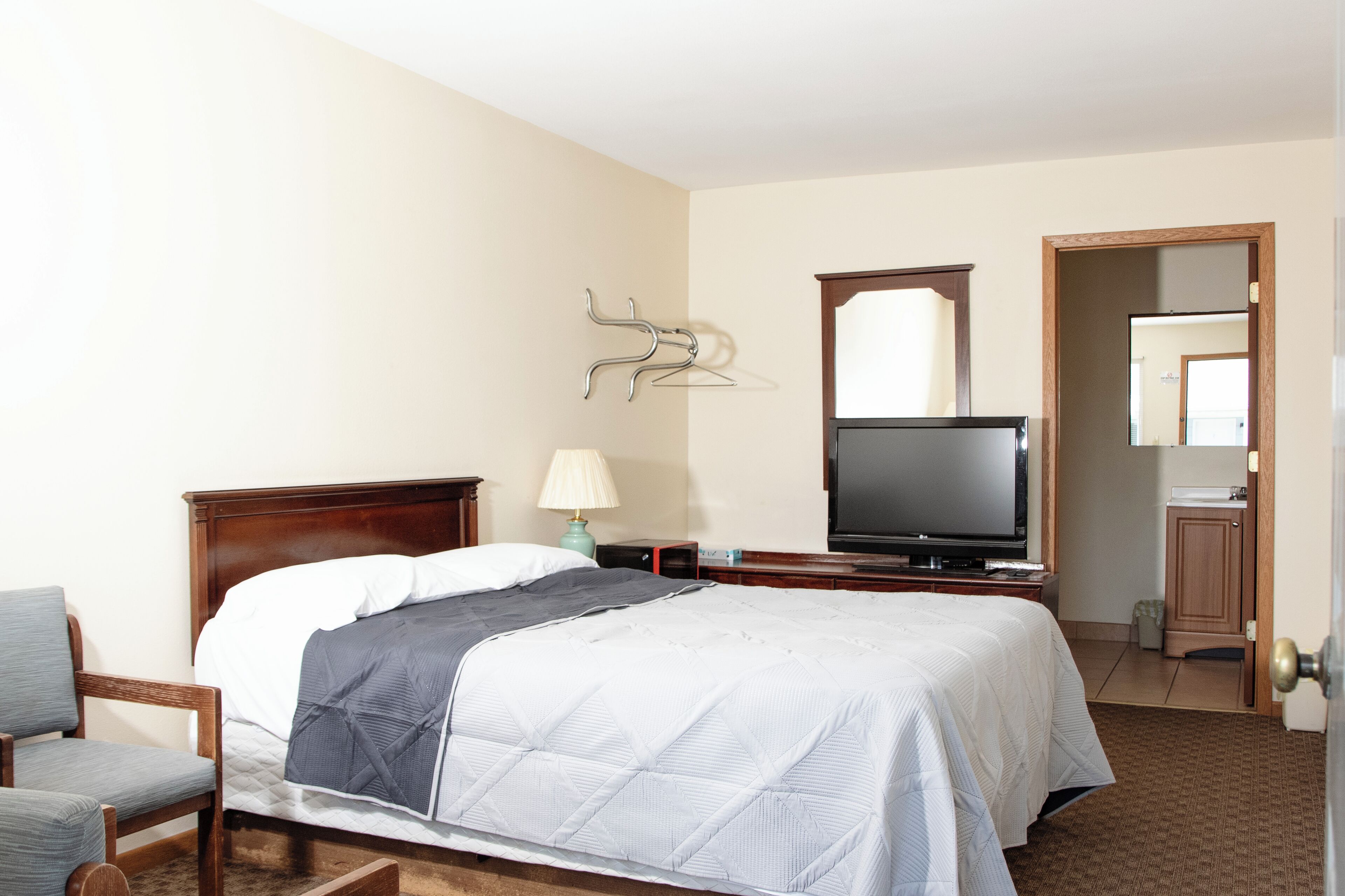 Une chambre d’hôtel avec un lit, une télévision, une chaise et un miroir.