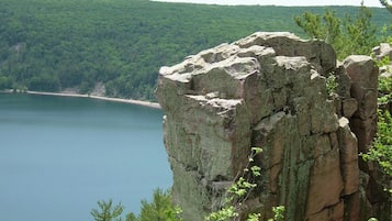 A natural landscape with a prominent rock formation overlooking a calm lake and dense forest.