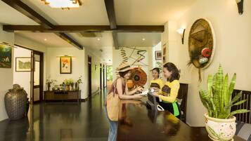 A reception area with a polished wooden reception desk, a large potted plant, and a wall-mounted decorative piece.