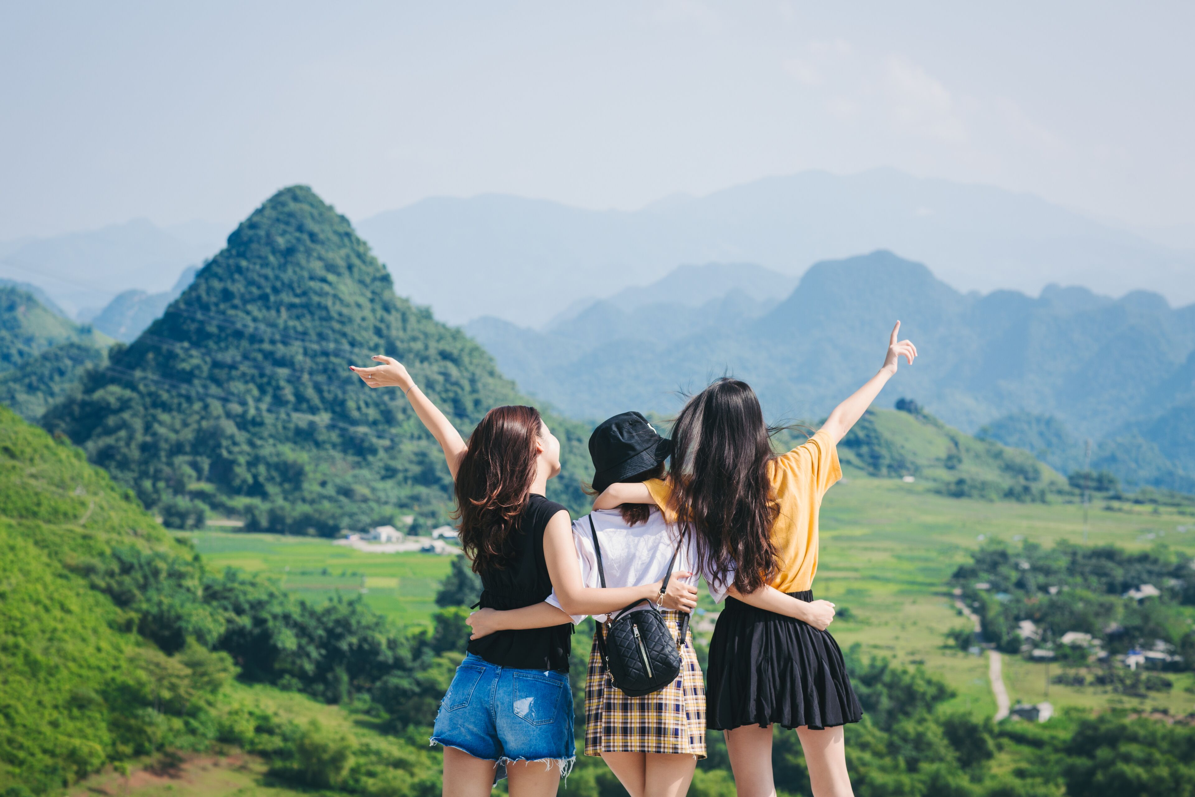 Three people standing on a hill with a mountainous landscape in the background.