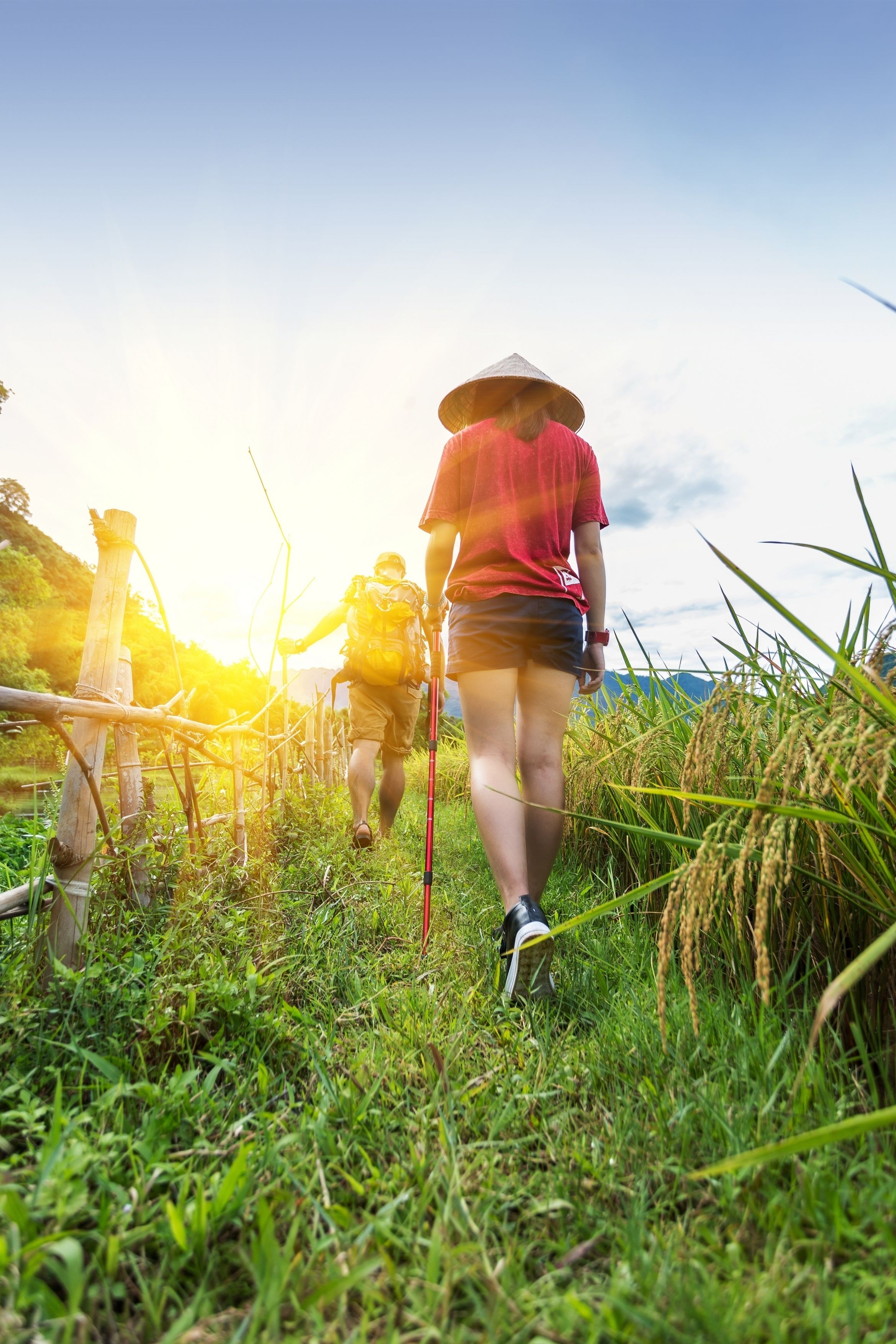 Due escursionisti camminano su un sentiero erboso con una recinzione in legno e l'erba alta ai lati.