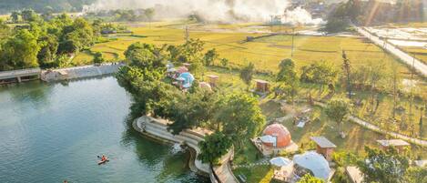 A riverside view with kayaks, a bridge, and a village with traditional houses and a large dome structure.