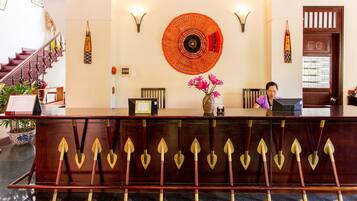 A reception desk with a wooden design, a large circular wall hanging, and a staircase in the background.