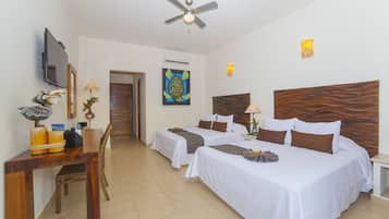 A hotel room with two beds, a desk with a chair, a ceiling fan, and a TV mounted on the wall.