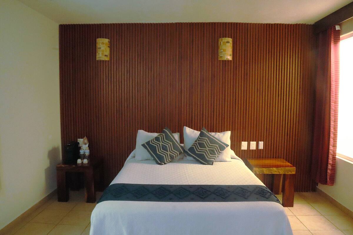 Une chambre d’hôtel avec un lit, deux oreillers, une table de chevet et une tête de lit en bois.