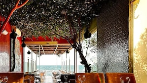 An outdoor dining area with tables and chairs, a view of the sea, and a covered walkway.