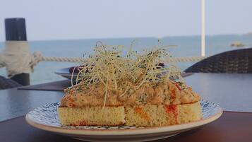 Een bord eten met een romige topping en geraspte garnering, op een tafel met uitzicht op zee.