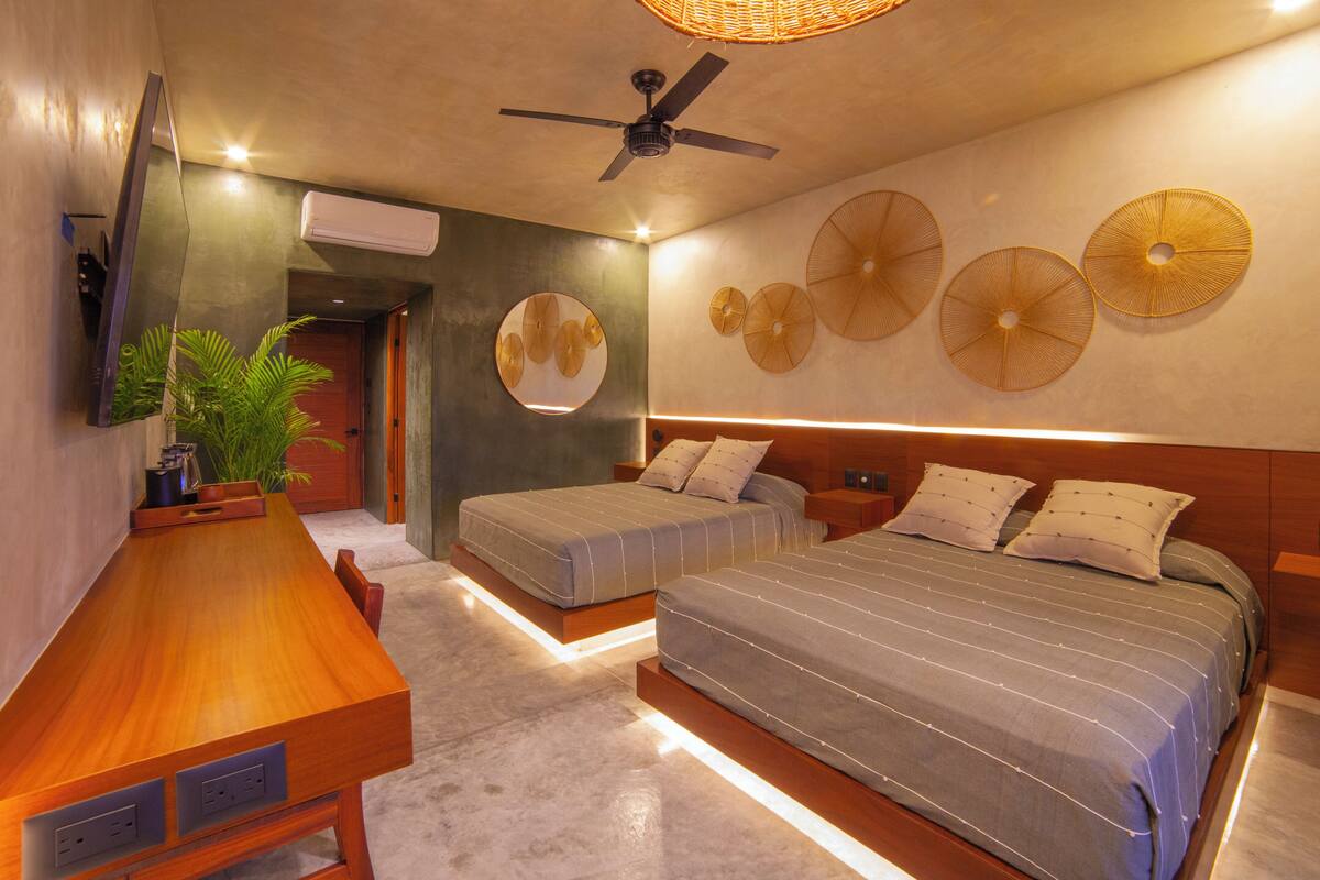 Une chambre moderne avec un bureau en bois, deux lits, un ventilateur de plafond et des éléments décoratifs fixés au mur.