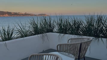 A terrace with wicker chairs and a view of the sea.