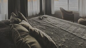 A room with a bed, a chair, and a view of the sea.