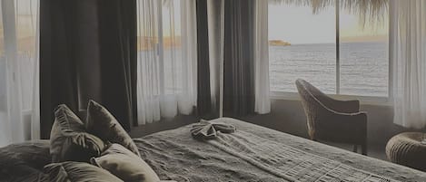 A room with a bed, a chair, and a view of the sea.