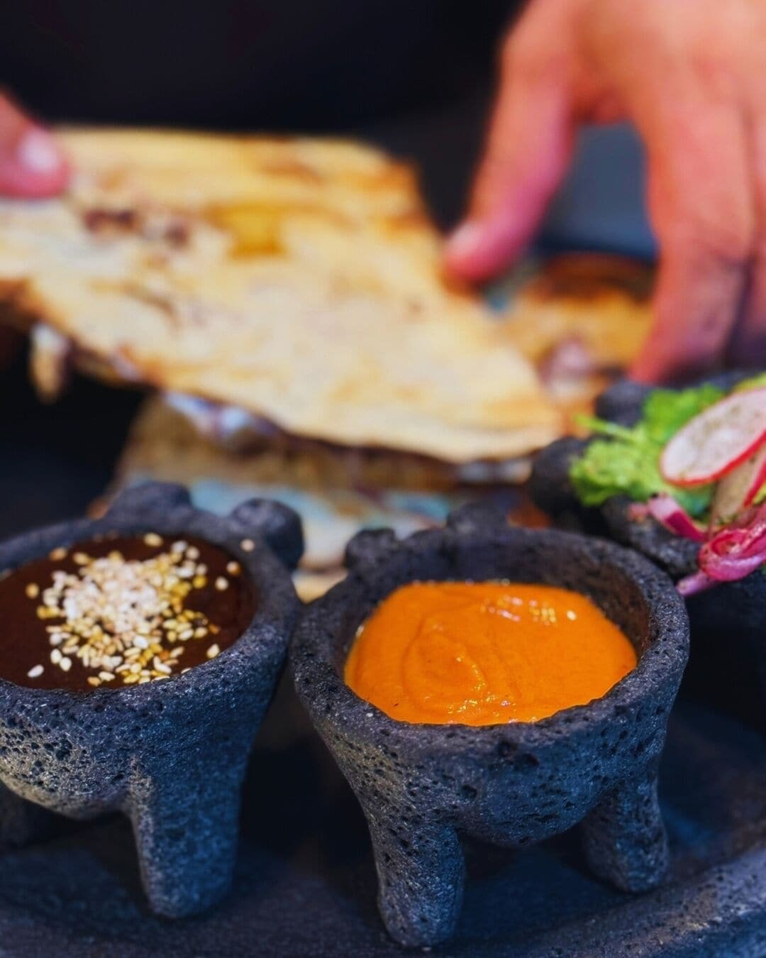 A close-up of a traditional Mexican dish with a tortilla and two small stone bowls containing sauces.