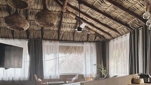 A room with a thatched ceiling, a bed, a desk, and a chair.