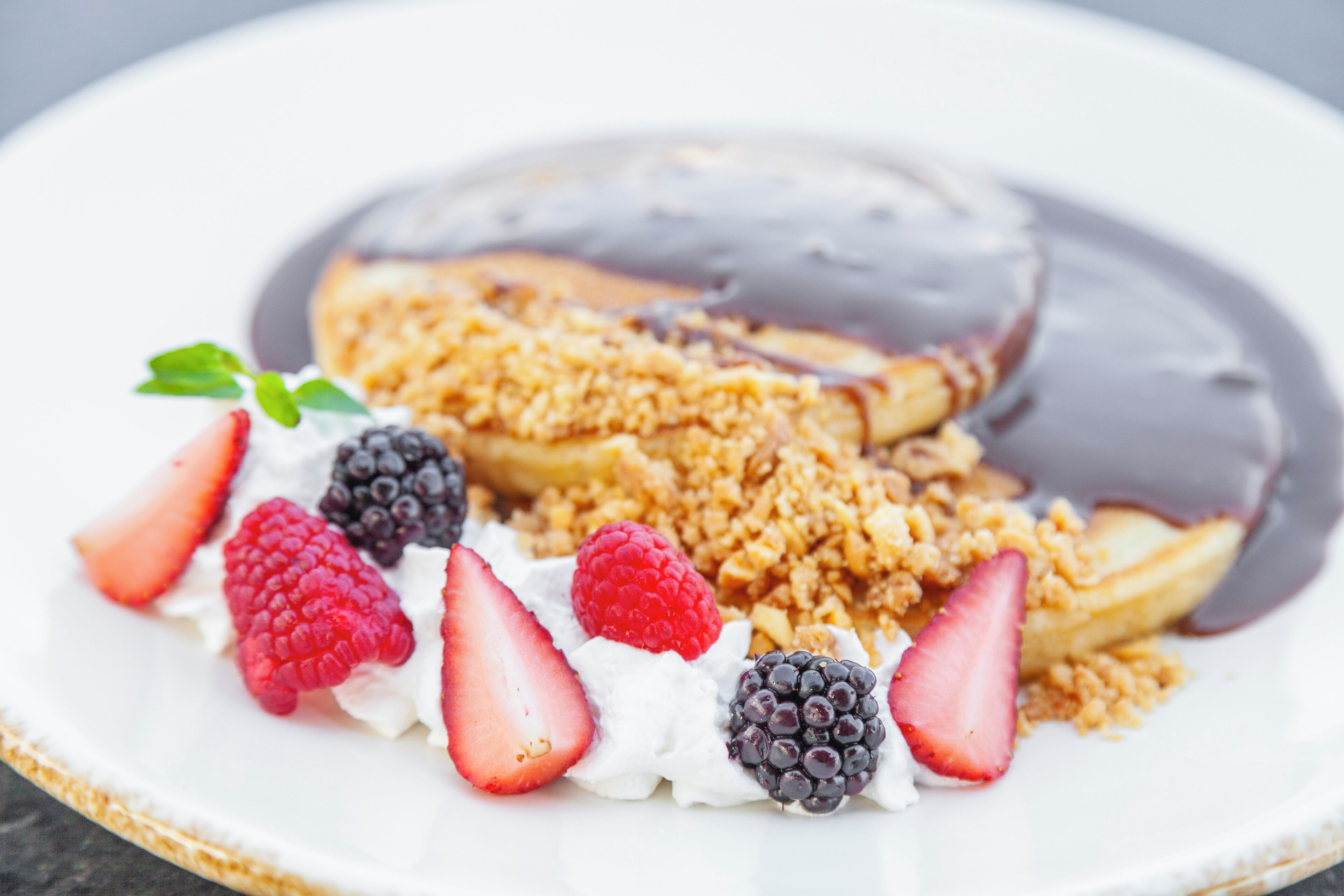 A dessert plate with a chocolate-covered pastry, whipped cream, strawberries, raspberries, and blackberries.