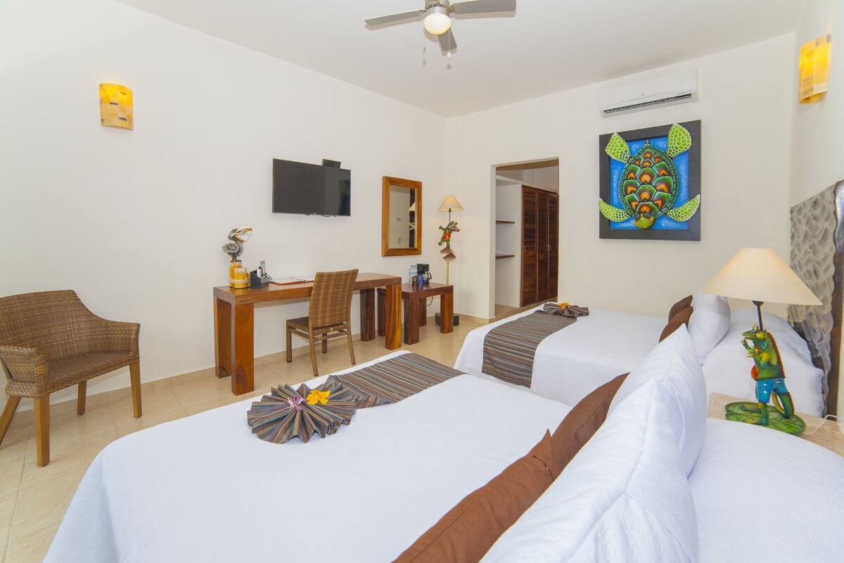 Une chambre d’hôtel avec deux lits, un bureau, une chaise, une télévision et des œuvres d’art accrochées aux murs.