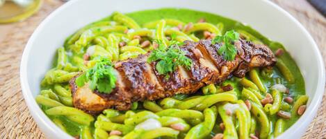 Eine Schüssel Pasta mit Fleisch und grüner Soße.