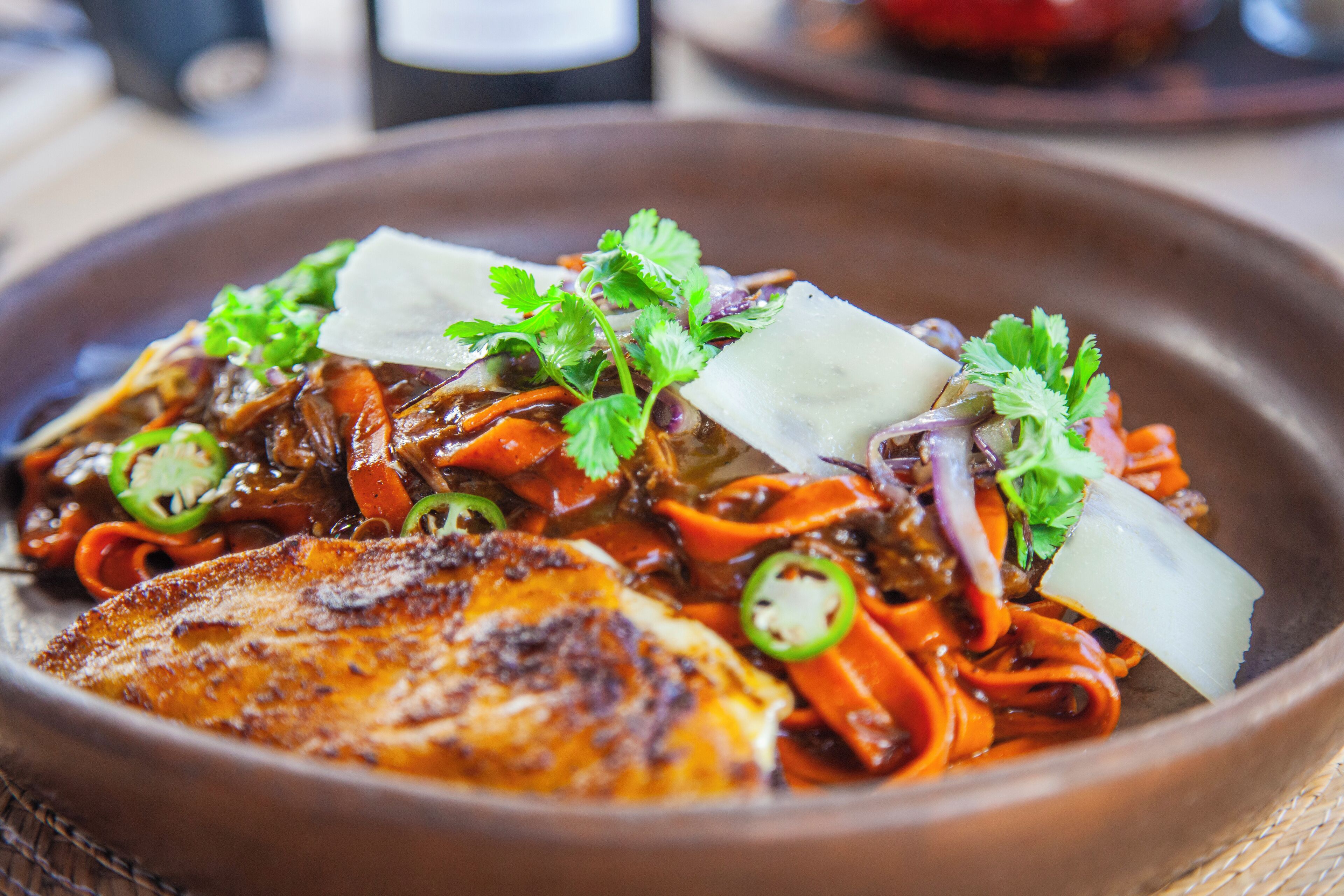 A dish with a piece of grilled chicken, vegetables, and garnishes in a bowl.