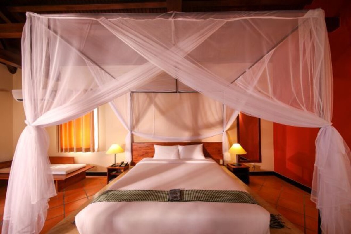 A room with a bed under a white canopy, wooden floors, and two bedside lamps.