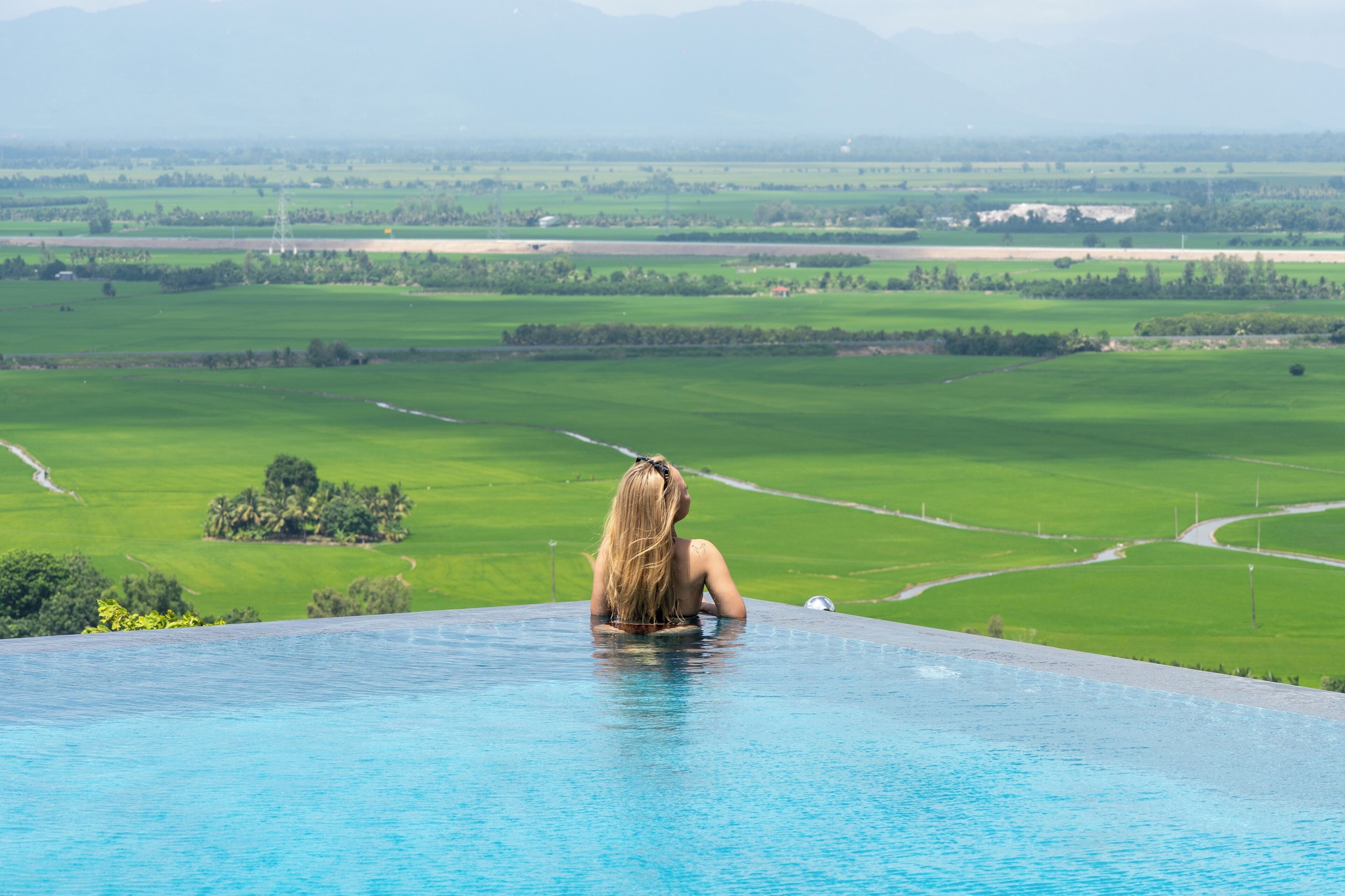 Una persona sentada en una piscina con vistas a un paisaje verde y montañas a lo lejos.
