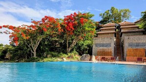 Piscina con agua azul cristalina, rodeada de exuberante follaje y árboles con flores rojas.