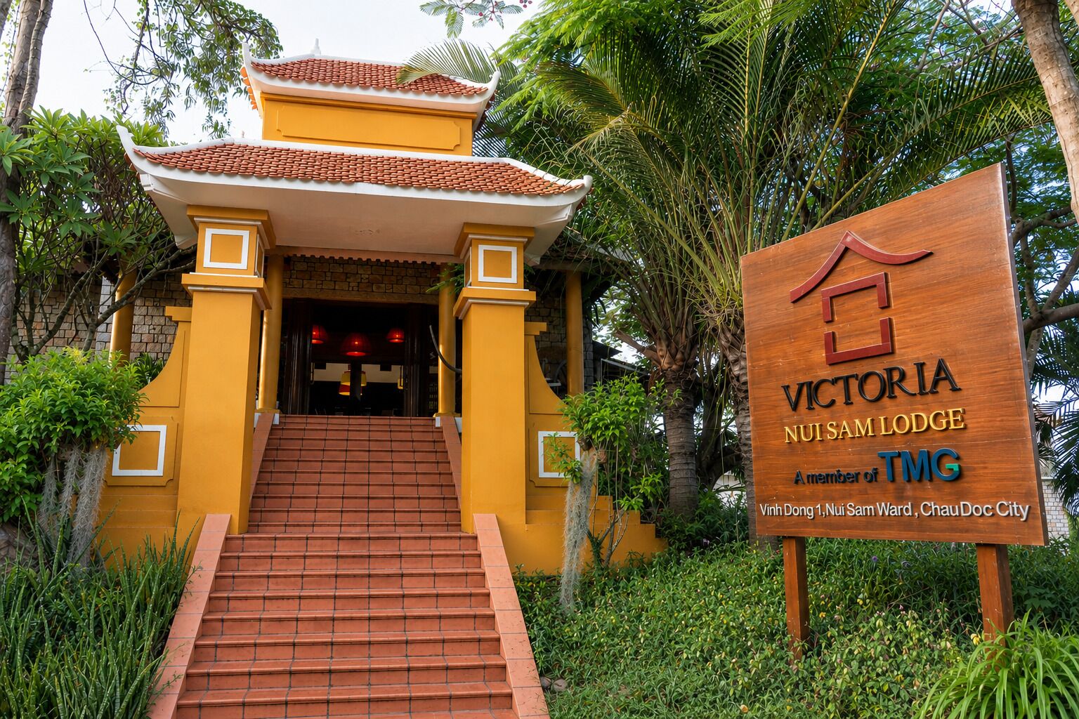 Señal de madera del Victoria Nui Sam Lodge con una entrada de arquitectura tradicional.