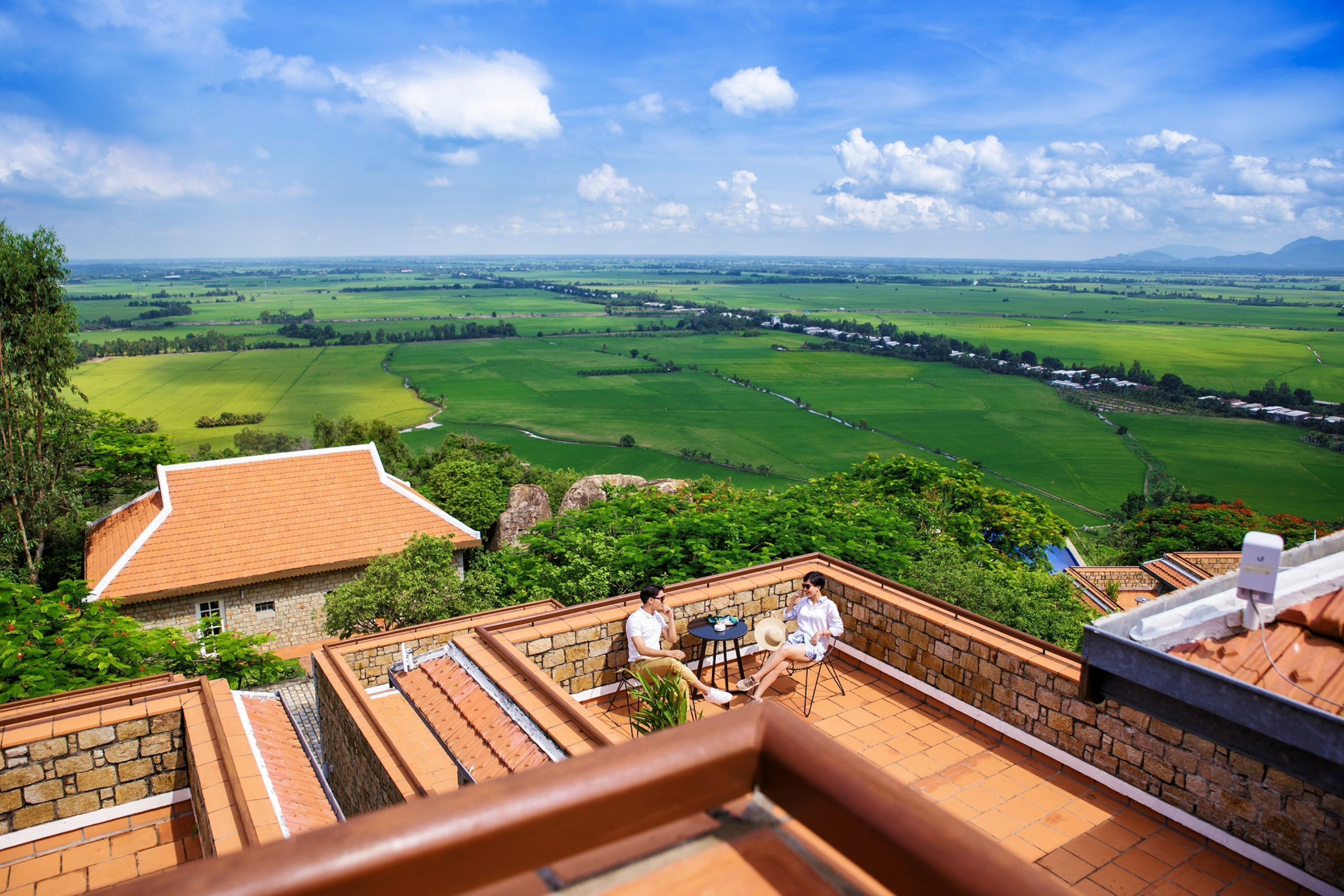 A terrace with a view of a green landscape, stone walls, and a tiled roof.