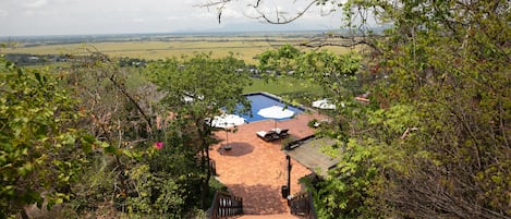 A brick pathway leading to a pool area surrounded by greenery, with a view of distant fields and mountains.