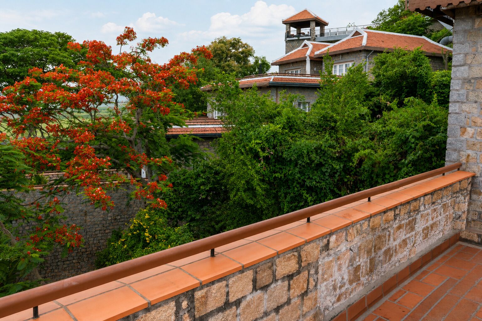 A stone balustrade overlooking a lush garden with a view of a building with a tiled roof.