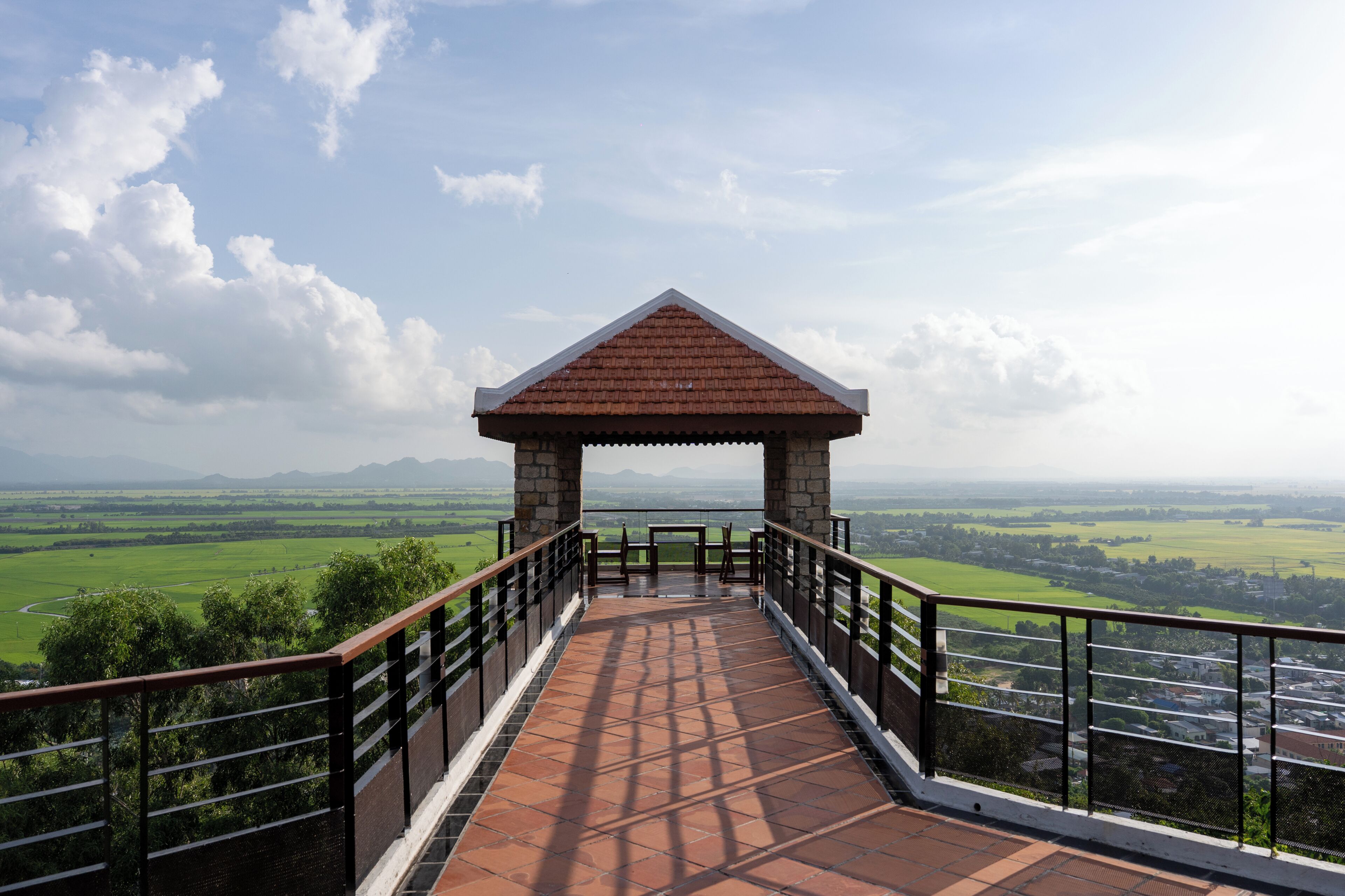 A pathway leading to a gazebo with a view of a green landscape and distant mountains.