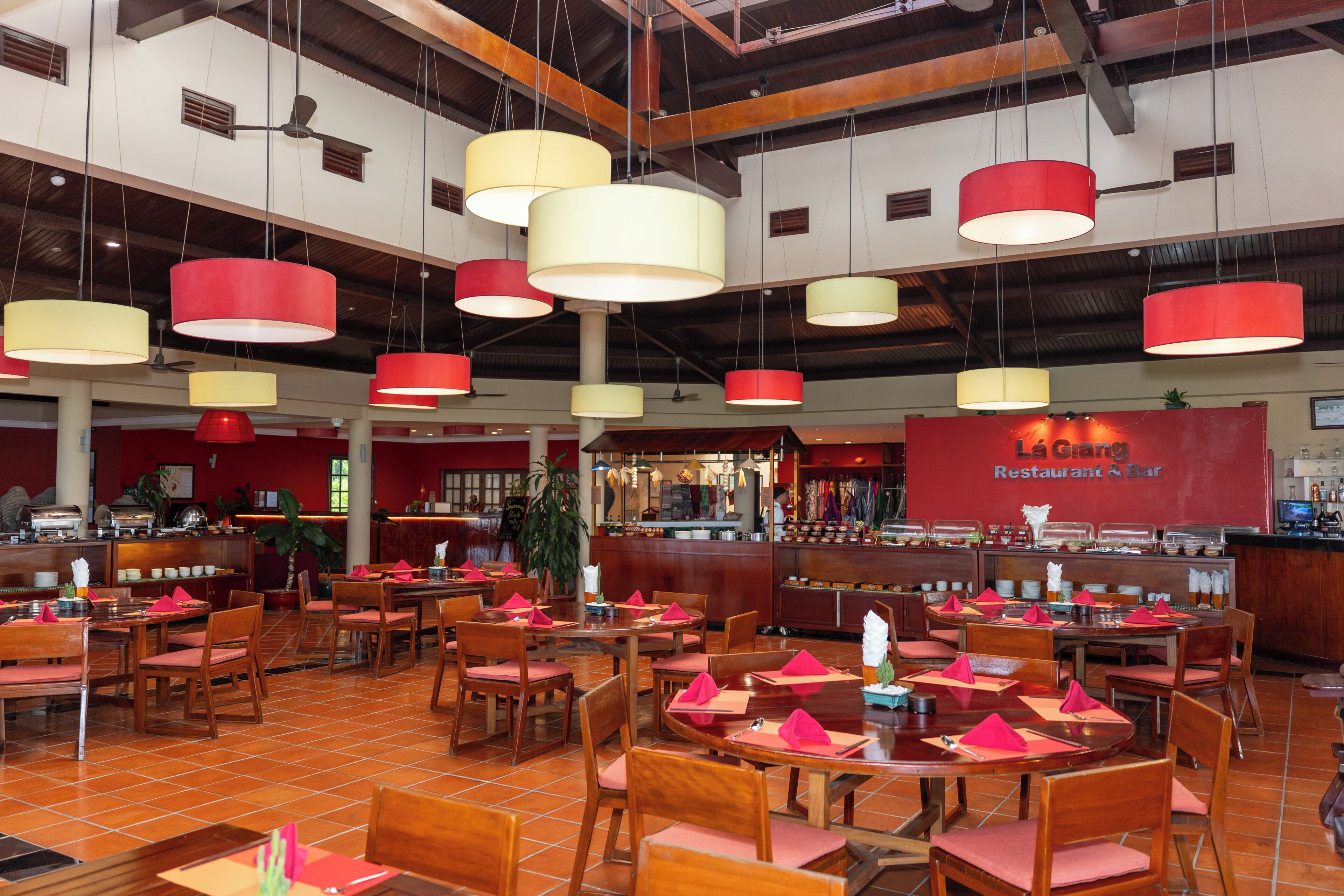 A restaurant with multiple dining tables and chairs, a bar area, and hanging pendant lights.