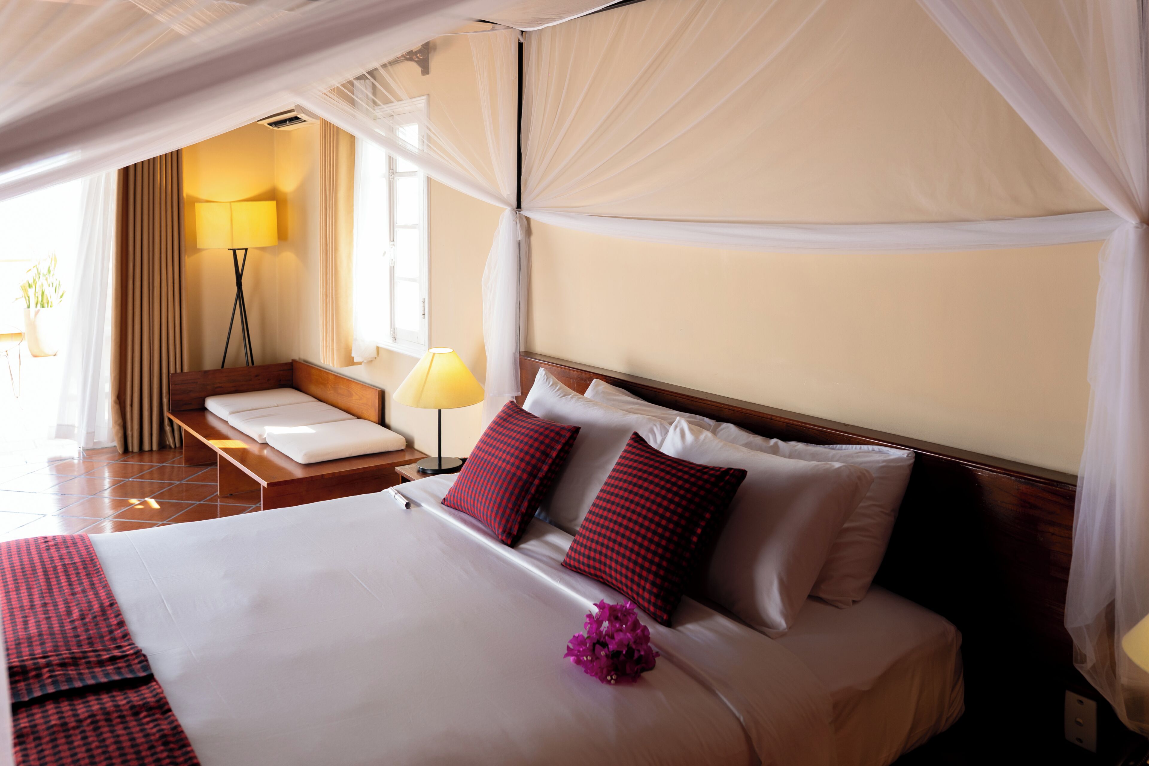 A hotel room with a bed, bedside tables, a lamp, and a view of the outdoors.