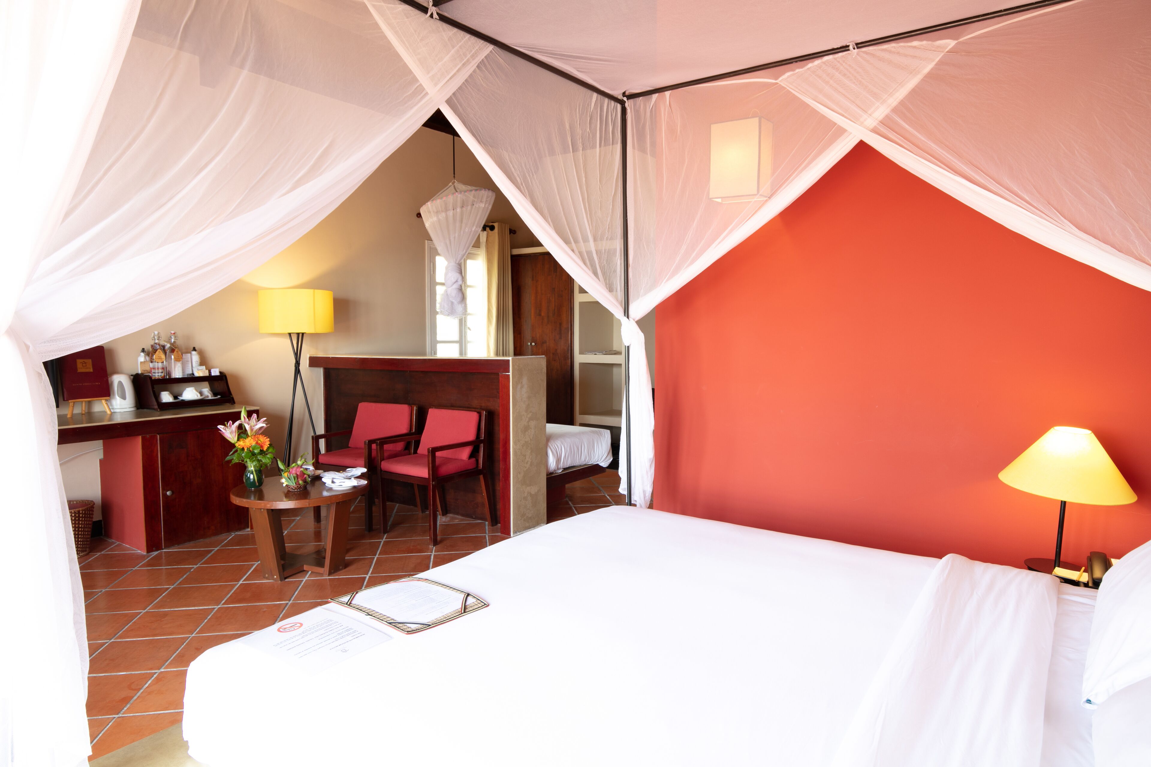 A hotel room with a bed, a desk, a chair, a lamp, and a red accent wall.